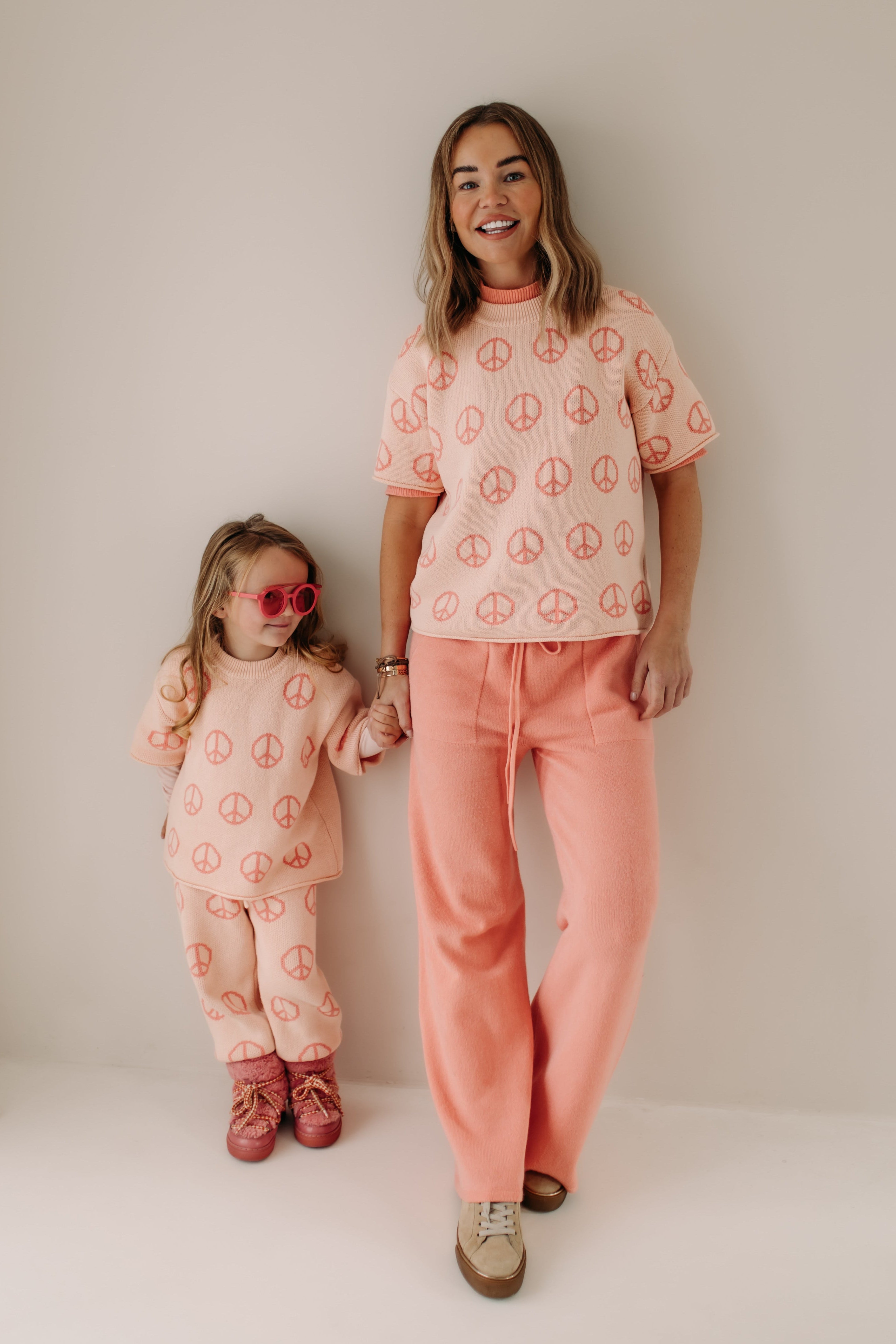 Woman and child wearing matching pink outfits with peace symbol prints on a white background